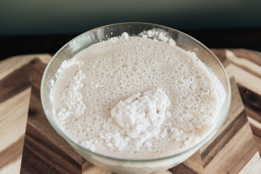 Image of a large glass bowl filled with yeast, warm water, and honey whisked to a foamy consistency for this focaccia recipe.