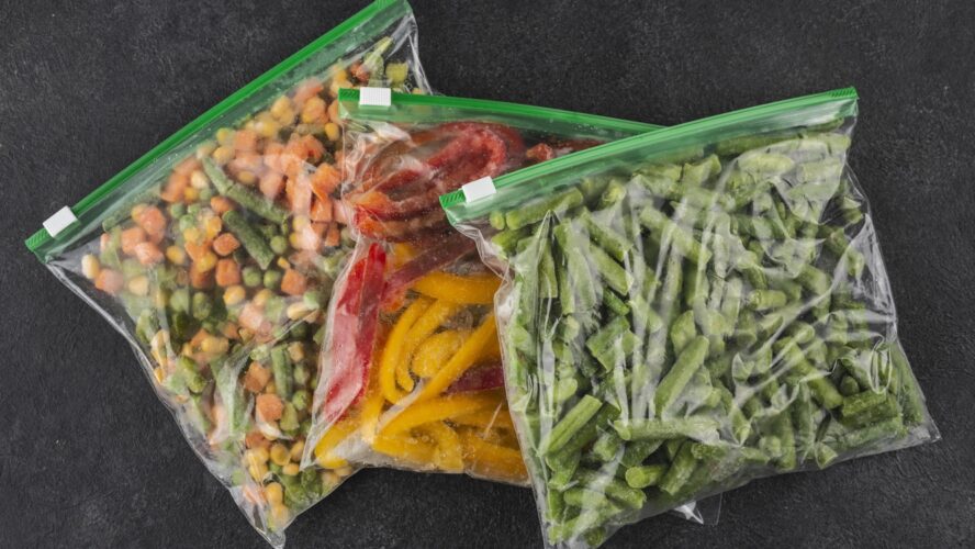 Image of three Ziploc bags filled with frozen vegetables set on a black marble counter.