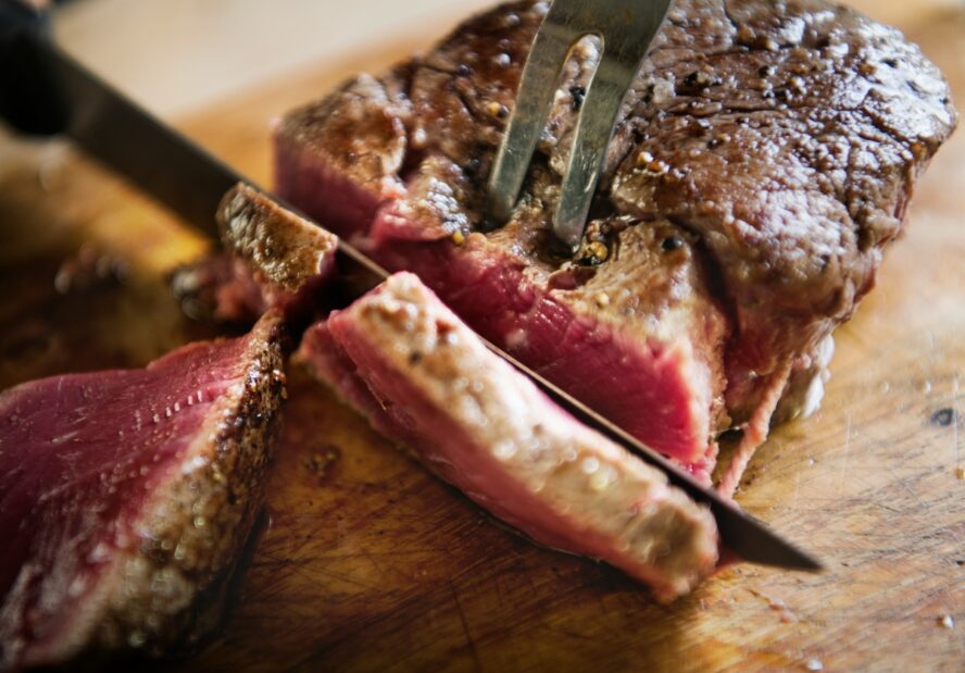 Image of a medium rare beef steak on a wooden board, cut into slices.