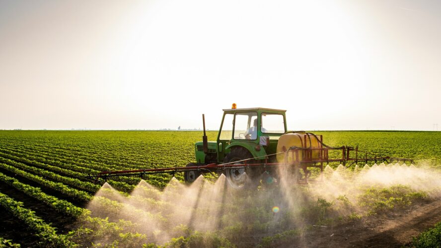 Image of a farmer in a tractor spraying organophosphate pesticides over a field of crops.