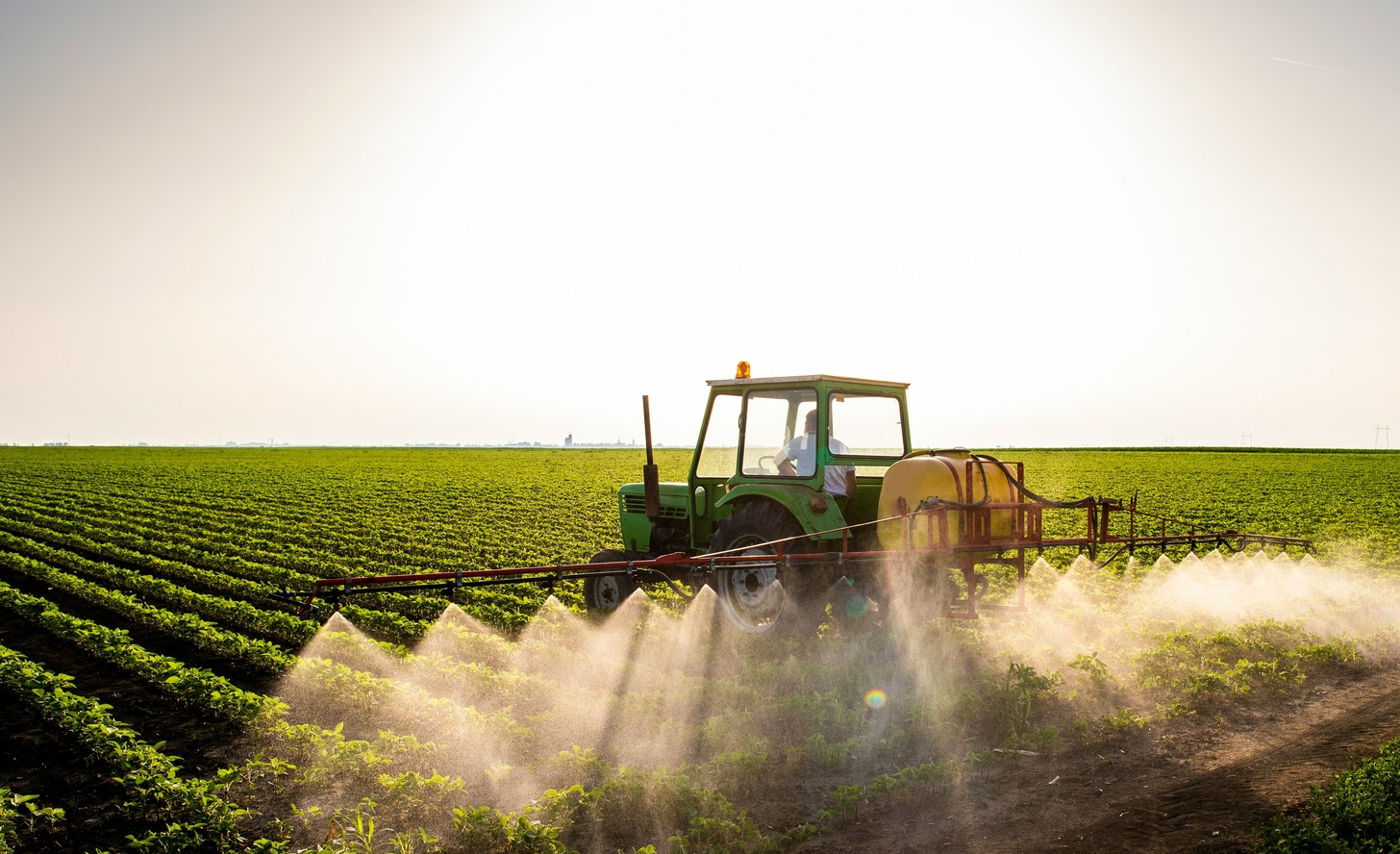 Image of a farmer in a tractor spraying organophosphate pesticides over a field of crops.