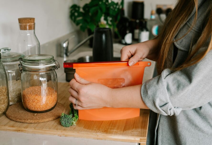 Image of a pair of hands sealing an orange reusable silicone freezer-safe bag.