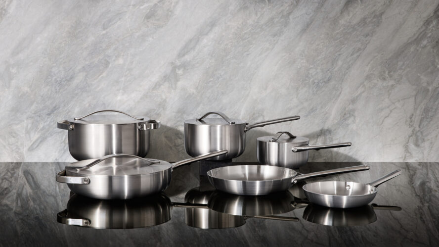 Image of a full Caraway Stainless Steel cookware set displayed on a black marble countertop.