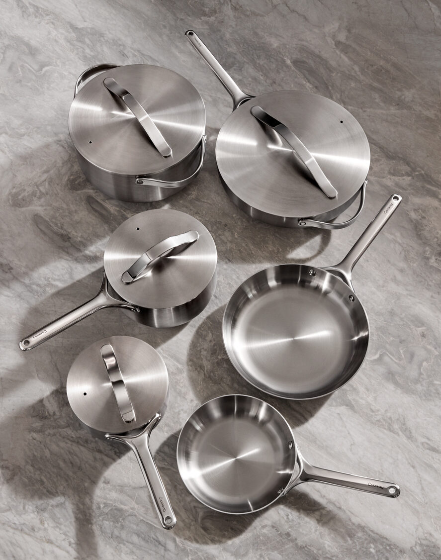 Image of several pieces in the Caraway Stainless Steel cookware set, including multiple fry pans, sauce pans, and more.