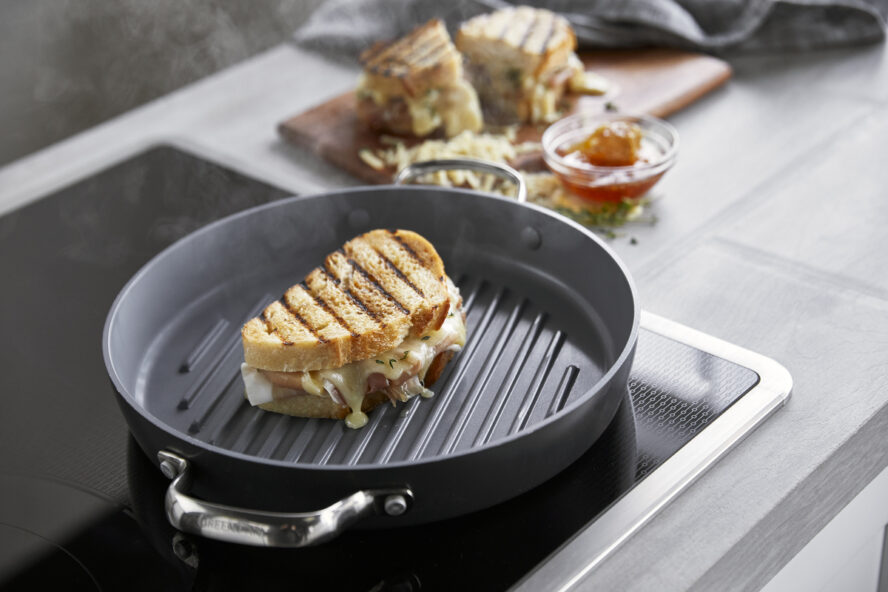 Image of the GreenPan Valencia Pro round grill pan on a stovetop being used to make a grilled cheese sandwich.