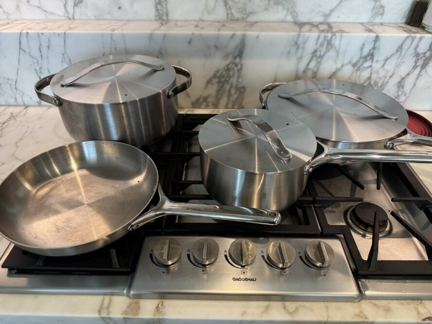 Image of several Caraway Stainless Steel cookware pieces displayed on a stovetop with a white marble backsplash.