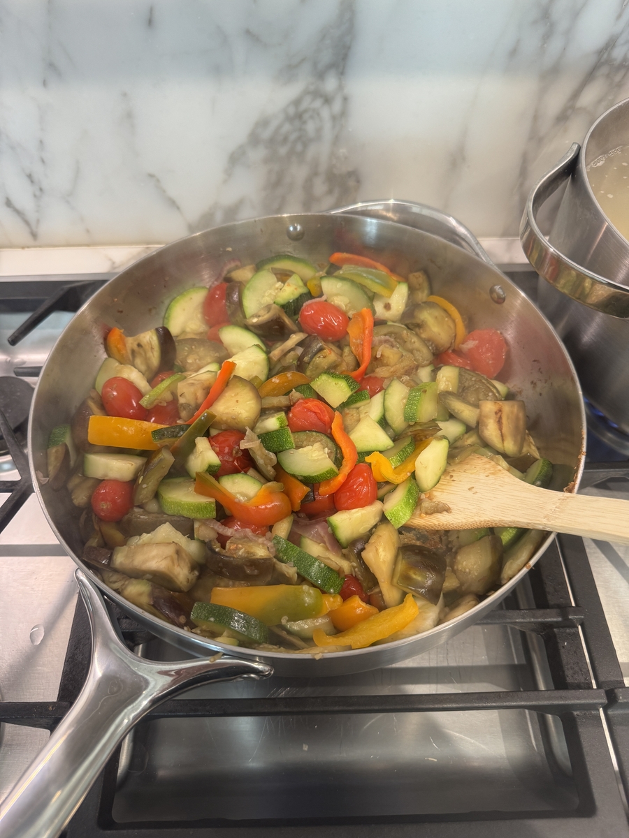 Image of the Caraway Stainless Steel Sauté Pan in action on a stovetop, filled with stir-fried veggies.