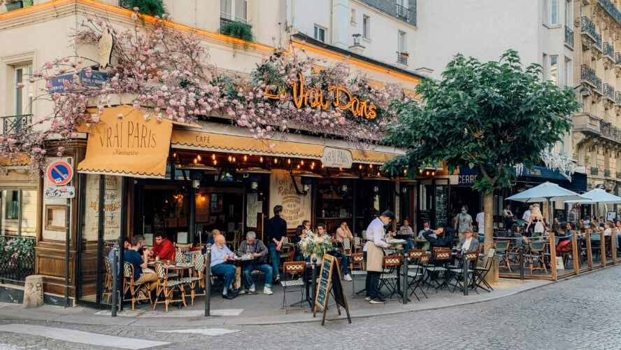 Image of a Parisian restaurant on a corner with outdoor seating and vines climbing up the walls.