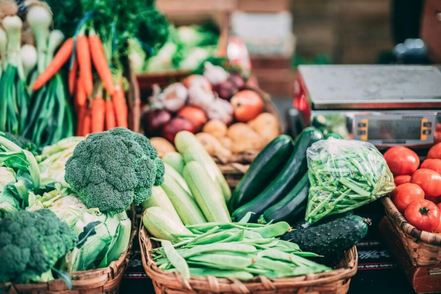 Image of several baskets full of high-fiber vegetables such as broccoli, zucchini, tomatoes, and more at a farmer's market table.
