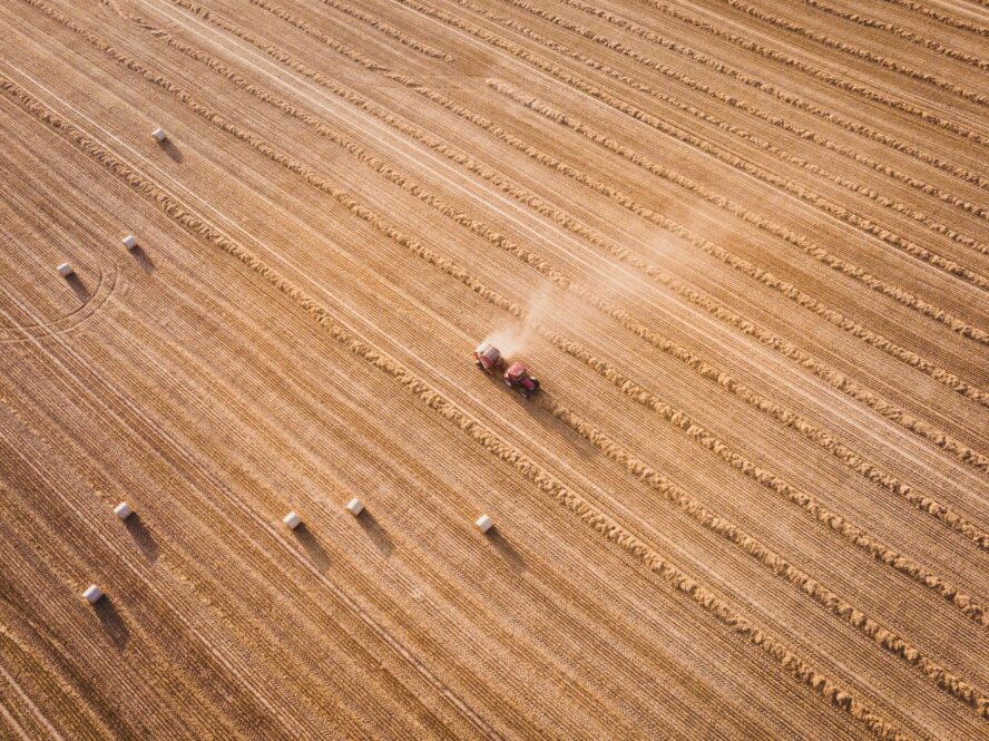 Overhead shot of a brown field of crops with tractors driving through and spraying herbicides.