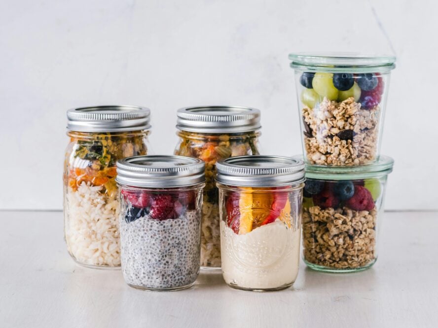 Image of glass mason jars filled up with various mixes of granola, chia seed puddings, fruits, and grain bowls.