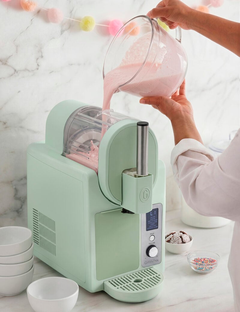 Image of a creamy pink liquid being poured into the clear mixing bowl at the top of the GreenPan Frost Pro ice cream maker in pistachio.