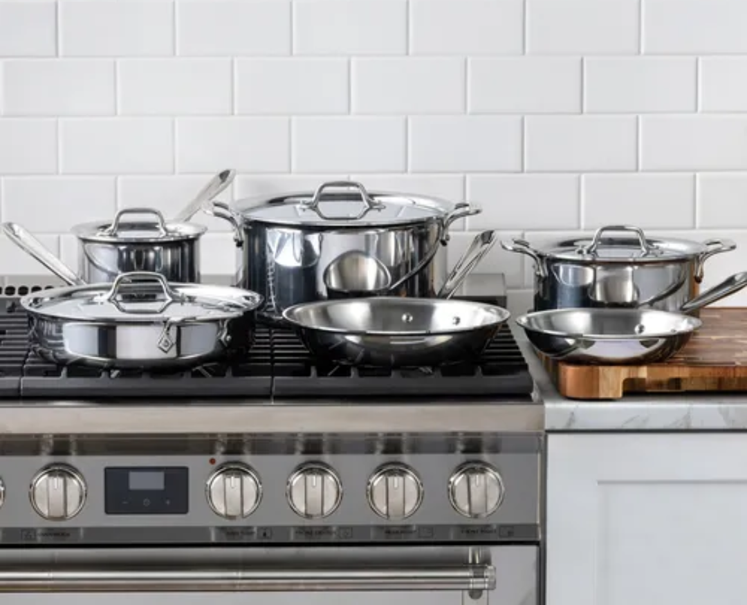 Image of the All-Clad D3 10-piece Stainless Steel set displayed on a gas stovetop in a brightly lit kitchen.