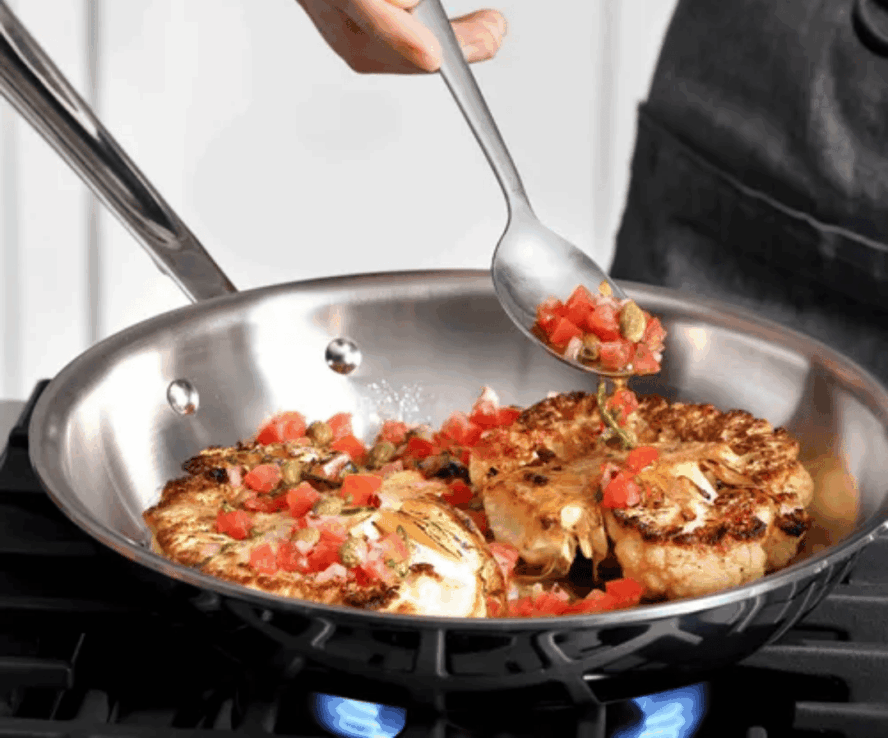Image of an All-Clad stainless steel pan being used to sear cauliflower with a bright romesco sauce.
