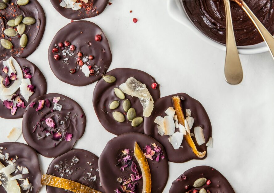 Image of dark chocolate bark bites sprinkled with nuts, orange peels, and pomegranate seeds.
