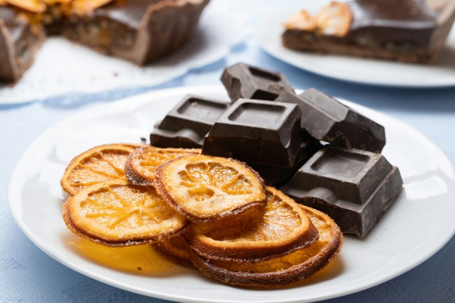 Image of a white plate with squares of dark chocolate next to dried oranges.