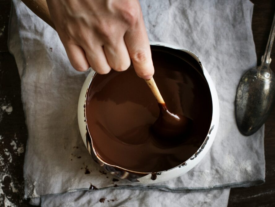 Image of a bowl of melted dark chocolate fondue, with a hand stirring a spoon in the chocolate sauce.