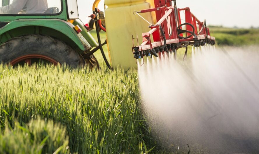 Close-up image of a tractor spraying pesticides over a field of grain crops.