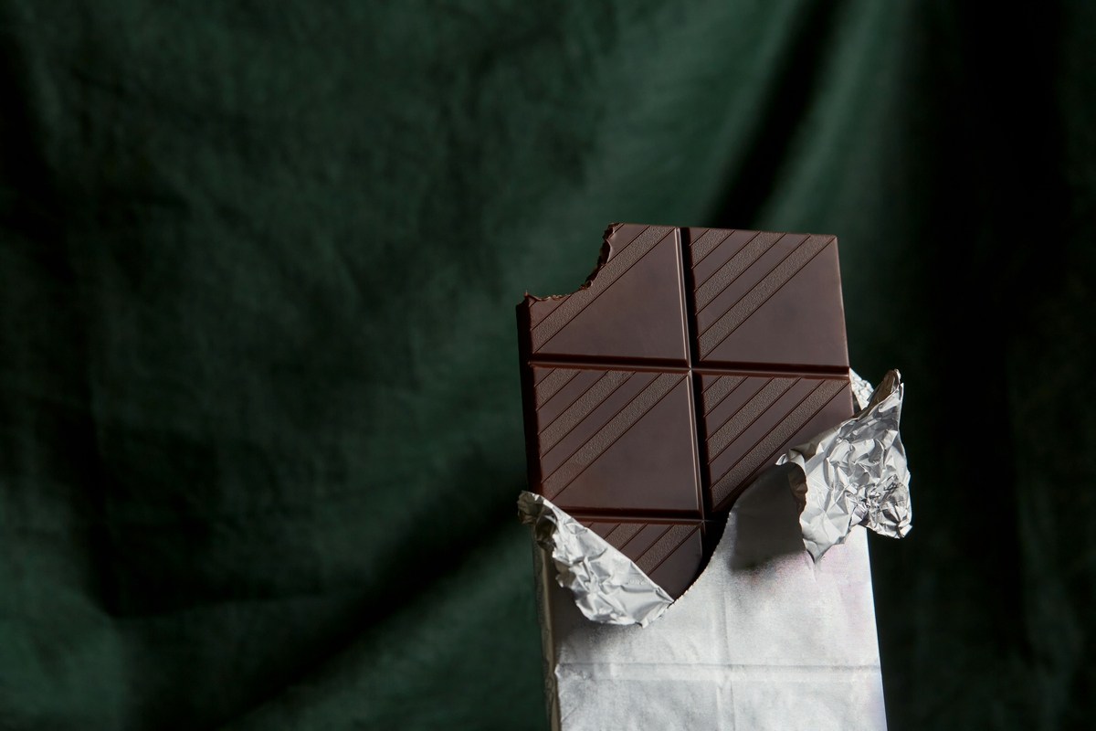 Image of a bar of dark chocolate in silver foil set against a dark green background.