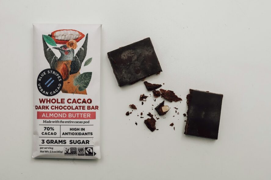Image of a wrapped bar of dark chocolate in its original packaging, with a few chunks of the chocolate displayed beside it.