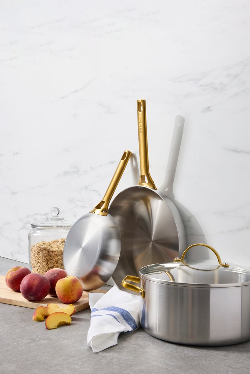 Three GreenPan Reserve Stainless Steel pieces displayed next to some peaches on a table.