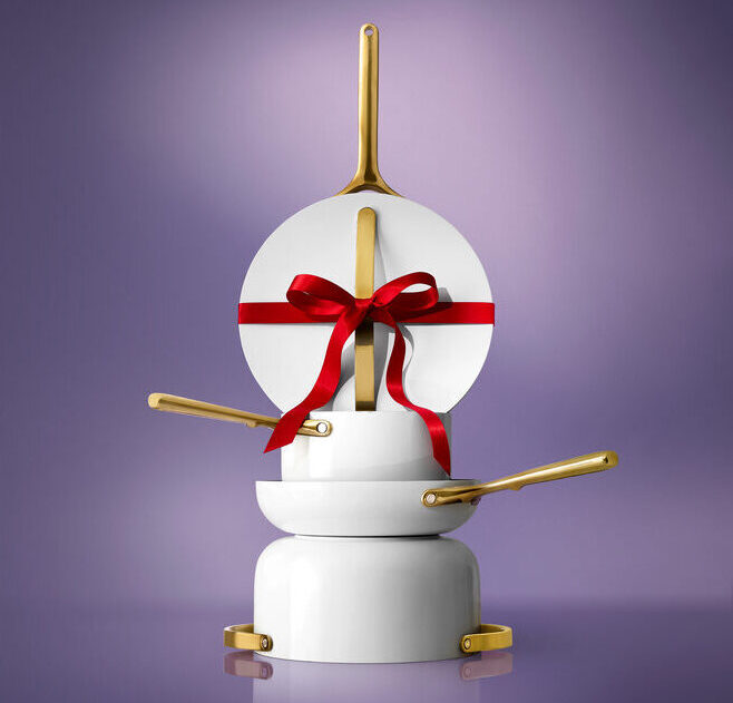 Image of a Caraway Cookware Set with gold handles, stacked in a pile with a red ribbon around one of the lids.