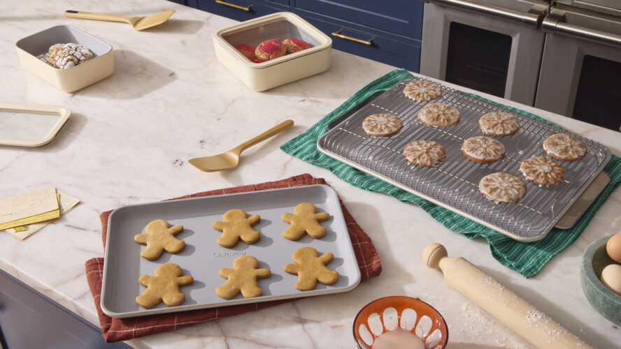 A festive spread featuring two Caraway baking sheets and a cooling rack with freshly baked holiday cookies.