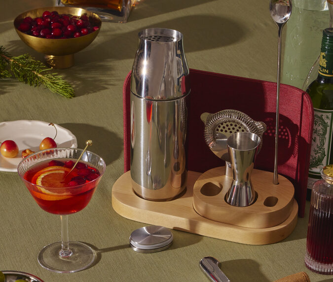 Lifestyle image of the Caraway Complete Bar Set on a green tablescape, being used to make bright red festive cocktails.