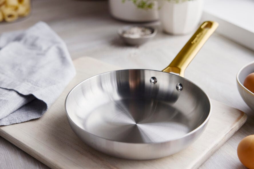 Image of a GreenPan Reserve Stainless Steel frypan displayed on a wooden cutting board in a brightly lit kitchen.