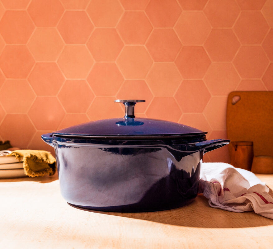Image of a Made In Dutch oven in a deep indigo colorway, set in a kitchen against terra cotta tiles.