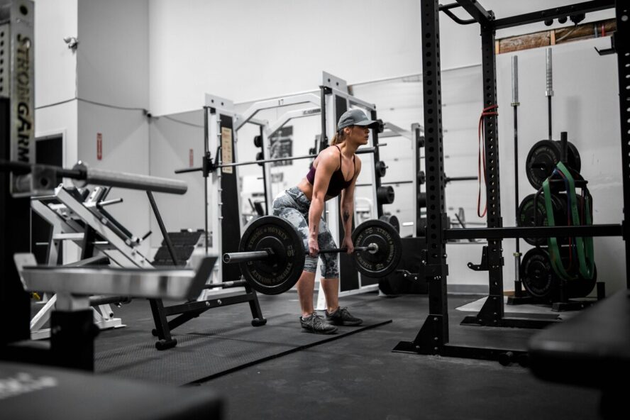 Image of a woman wearing a baseball cap and lifting a large barbell in an empty gym.
