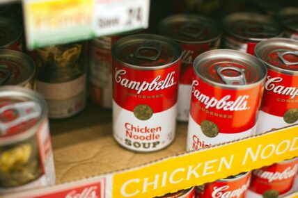 Image of a box on a grocery store shelf filled with Campbell's chicken noodle soup cans.