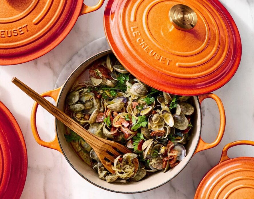 Image of an enameled Le Creuset Dutch oven in a gorgeous orange color being used for a stewed mussels dish.