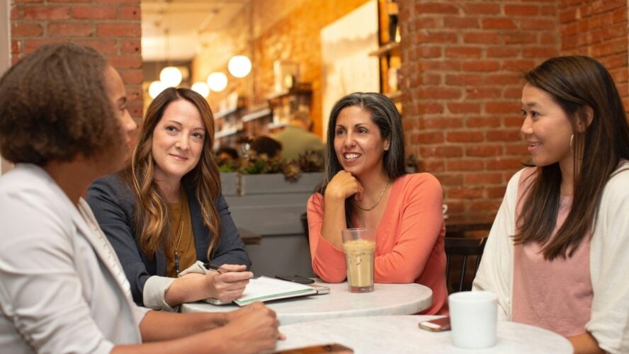 Image of four women sitting around a table at a cafe and chatting.