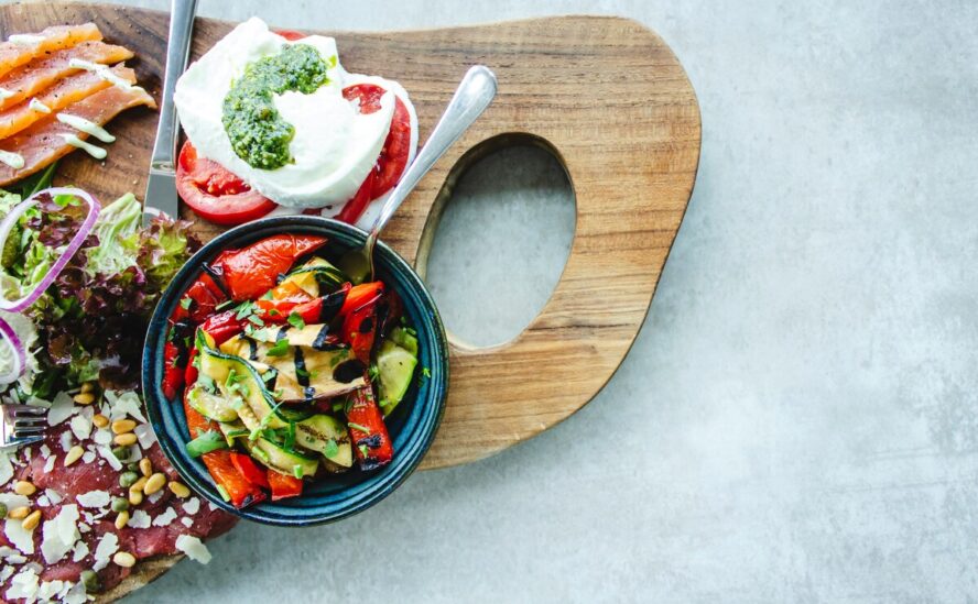 A gorgeous wooden board covered in colorful foods within the Mediterranean diet, including roasted vegetables, cheese, and fish.
