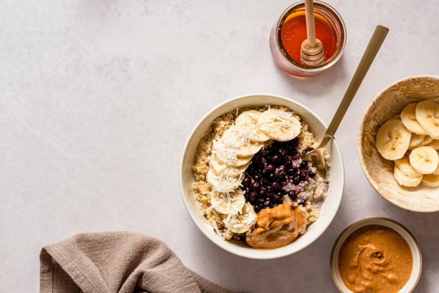 Image of a breakfast bowl of overnight oats topped with slices of banana, peanut butter, berries, and honey.