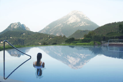 Image of a woman wading into an infinity pool overlooking the mountains of the Eastern Alps.