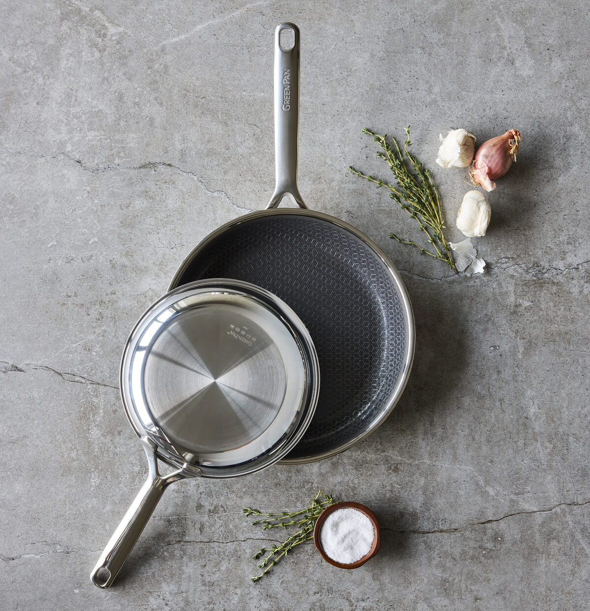 Image of two GreenPan Spectra Hybrid frying pans, the smaller one resting on top of the larger one against a grey marble backdrop.