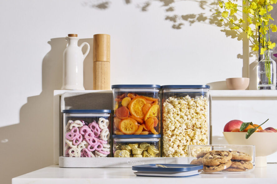 Image of the Caraway Glass Airtight Container set with navy lids, shown on a countertop full of pantry snacks.