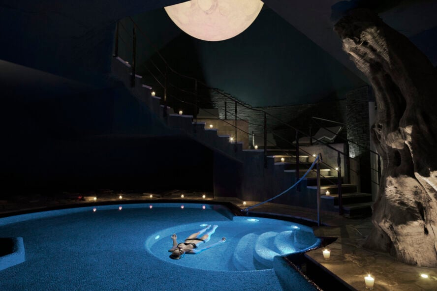 Image of a woman floating on her back in a dark saltwater pool lit by candles.
