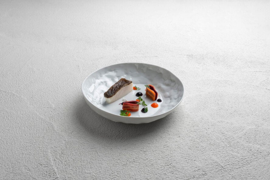 Image of a small plate with a beautifully arranged fish fine dining dish on it.