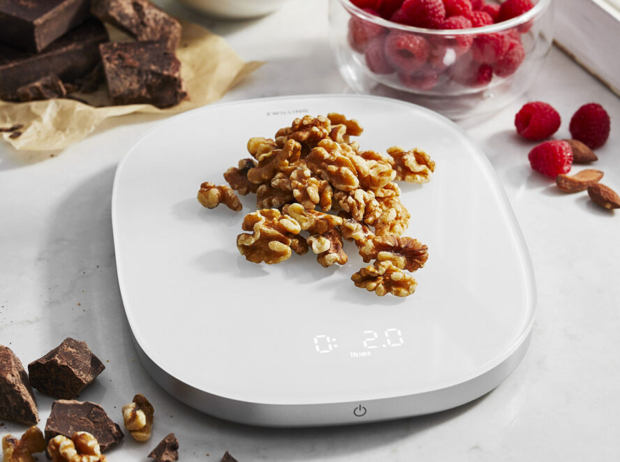 Image of the Zwilling digital food scale on a marble countertop with a handful of pecans on top of it.