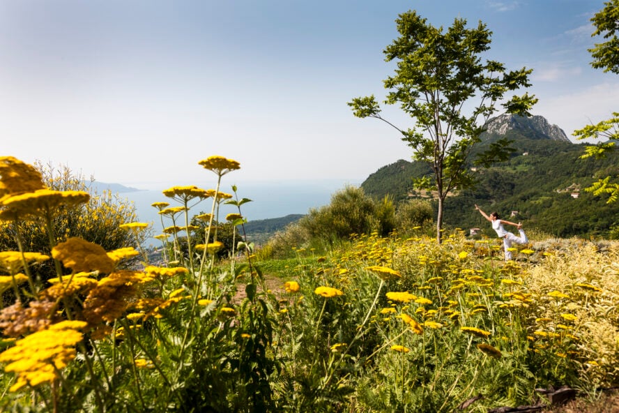 Image of the park at Lefay Resort & Spa overlooking Lake Garda, with a field of flowers and a woman doing yoga.