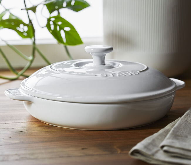 Image of the Staub Round Covered Brie Baker in pure white, shown on a wooden table.
