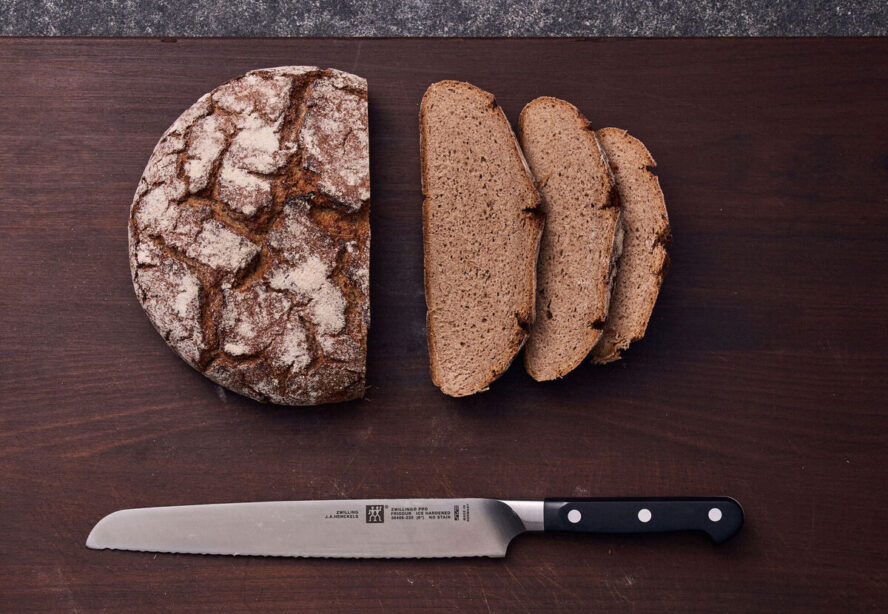 Image of a wooden slab with a loaf of whole wheat sourdough bread in slices next to the Zwilling Pro Bread Knife Z15 Serration.