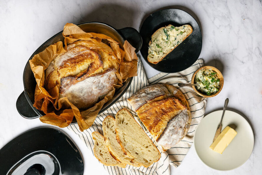 Image of the Xtrema Oval Dutch Oven with a large loaf of sourdough and a full spread of slices and butter around it.