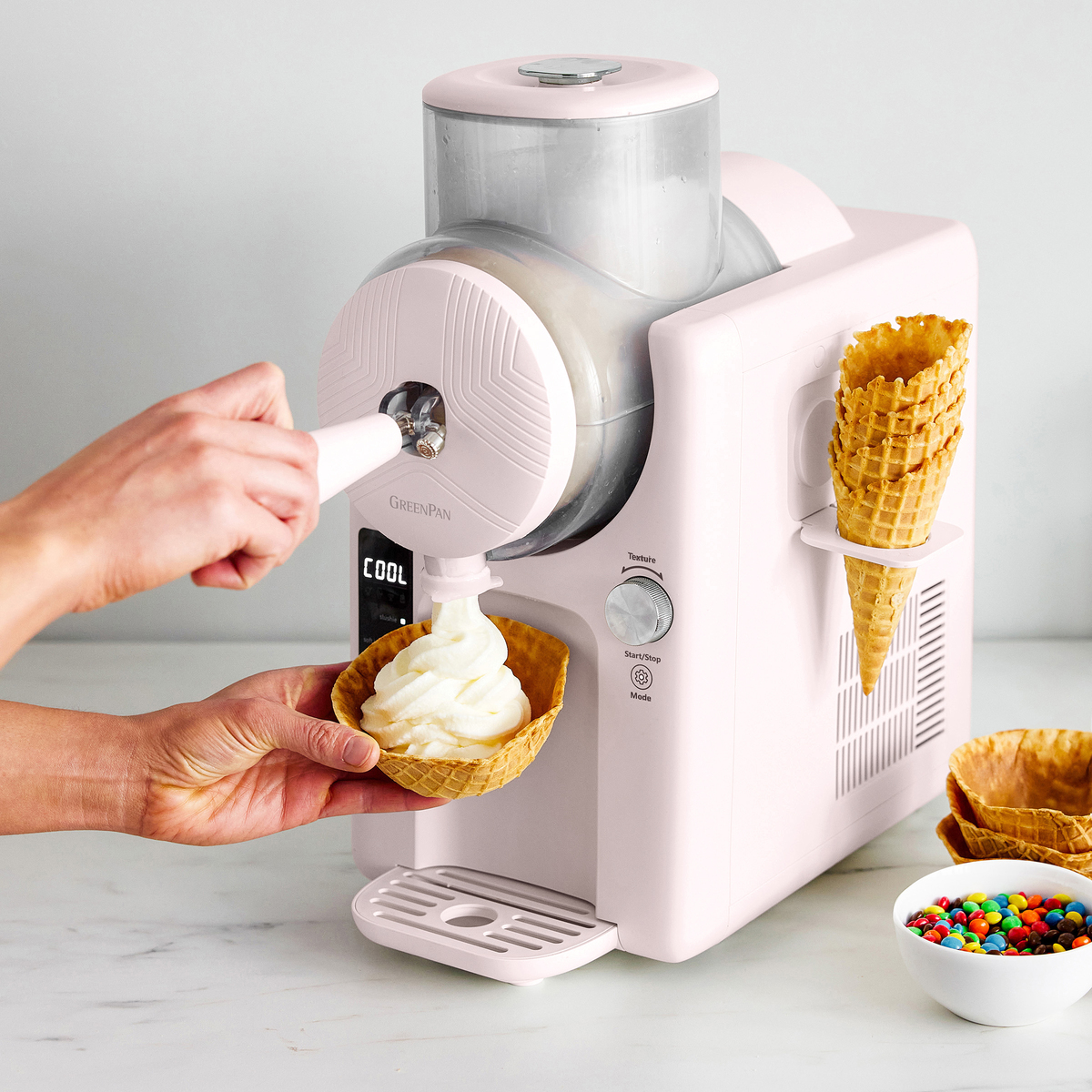 Image of the GreenPan Frost in Pink, with a pair of hands dispensing a swirl of soft serve into a waffle cone. 