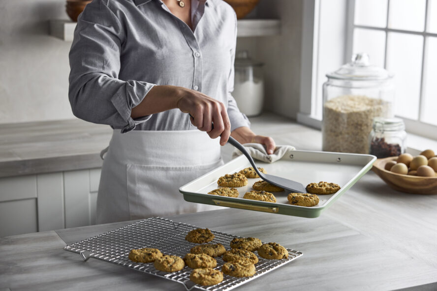 Image of a woman taking fresh cookies off of a GreenPan Reserve sheet pan in Sage Green.