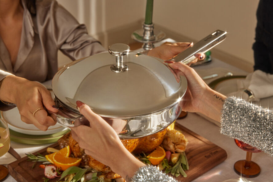 Image of the Our Place Titanium Always Pan Pro being passed over a holiday table spread.