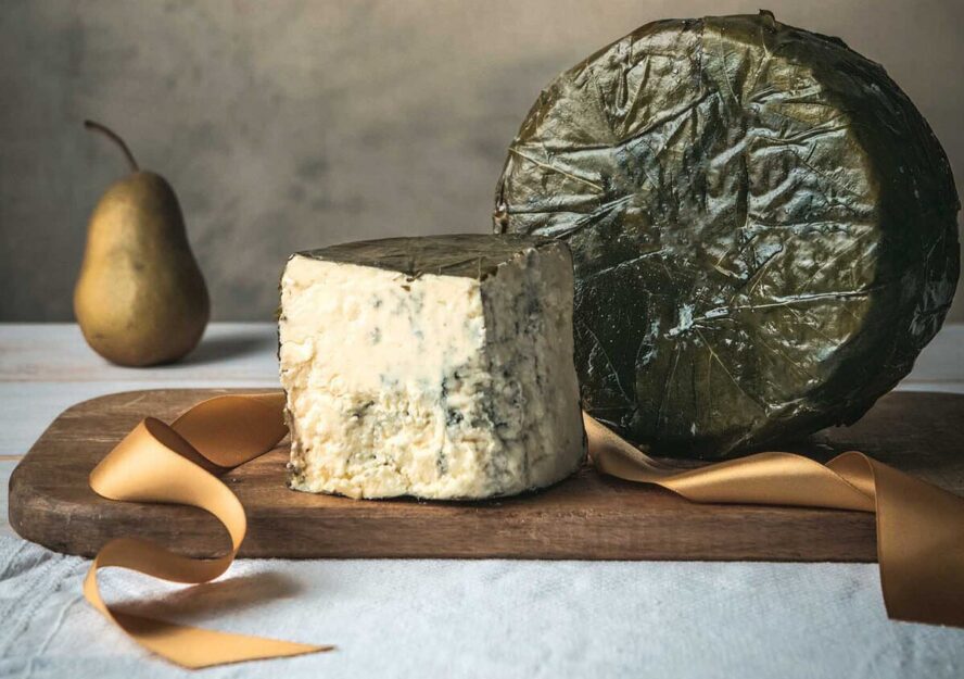 Image of Rogue Creamery's famous Rogue River Blue cheese, displayed as a wedge on a board next to a full wrapped round and a golden ribbon.